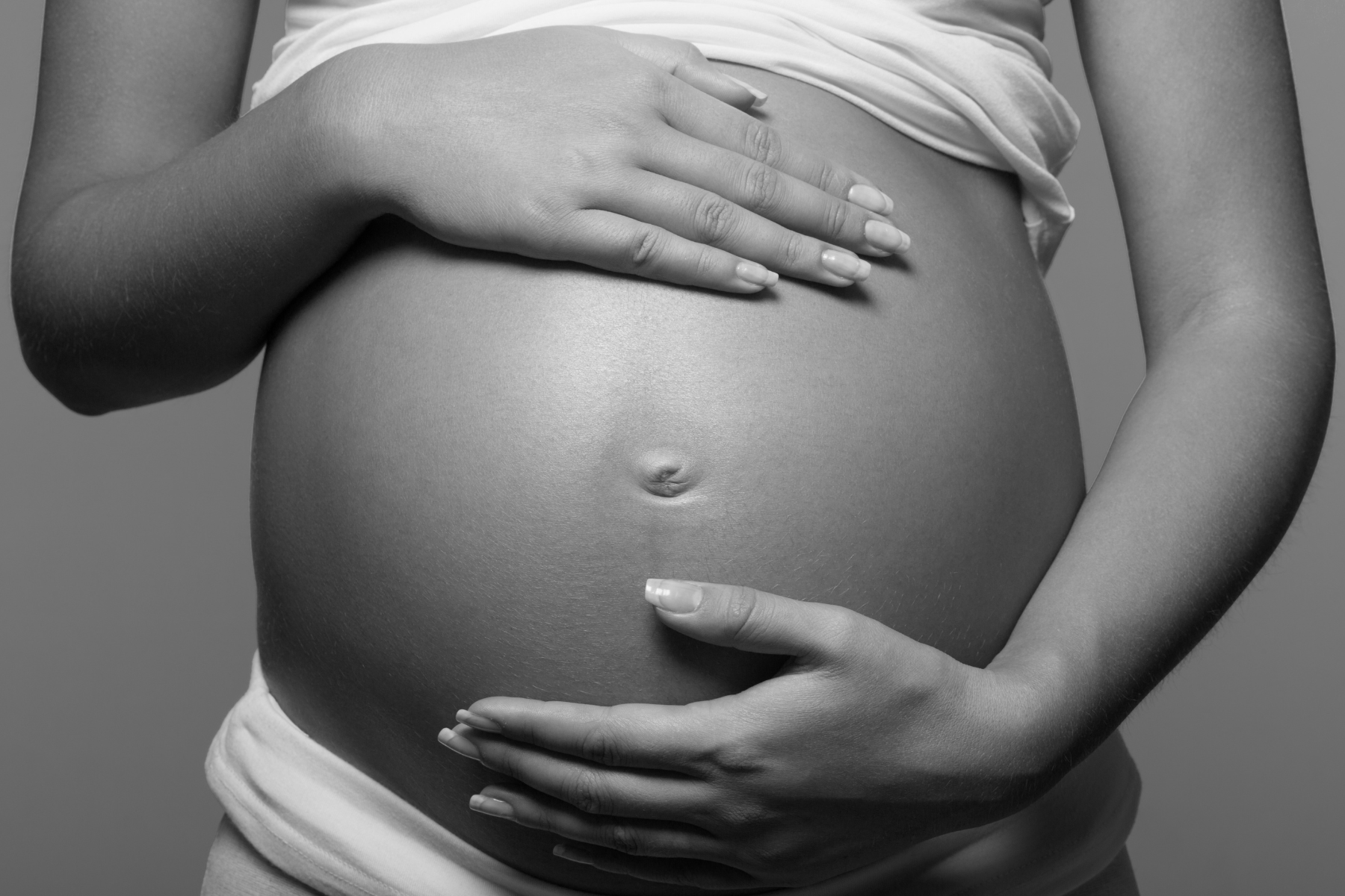 Black and white shot of hands holding pregnant belly.